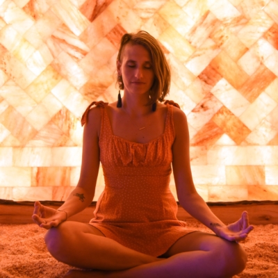 Woman Meditating On A Salt-Covered Floor In Front Of A Led Backlit Salt Panel Wall At The Prana Salt Cave - Wilmington, North Carolina.