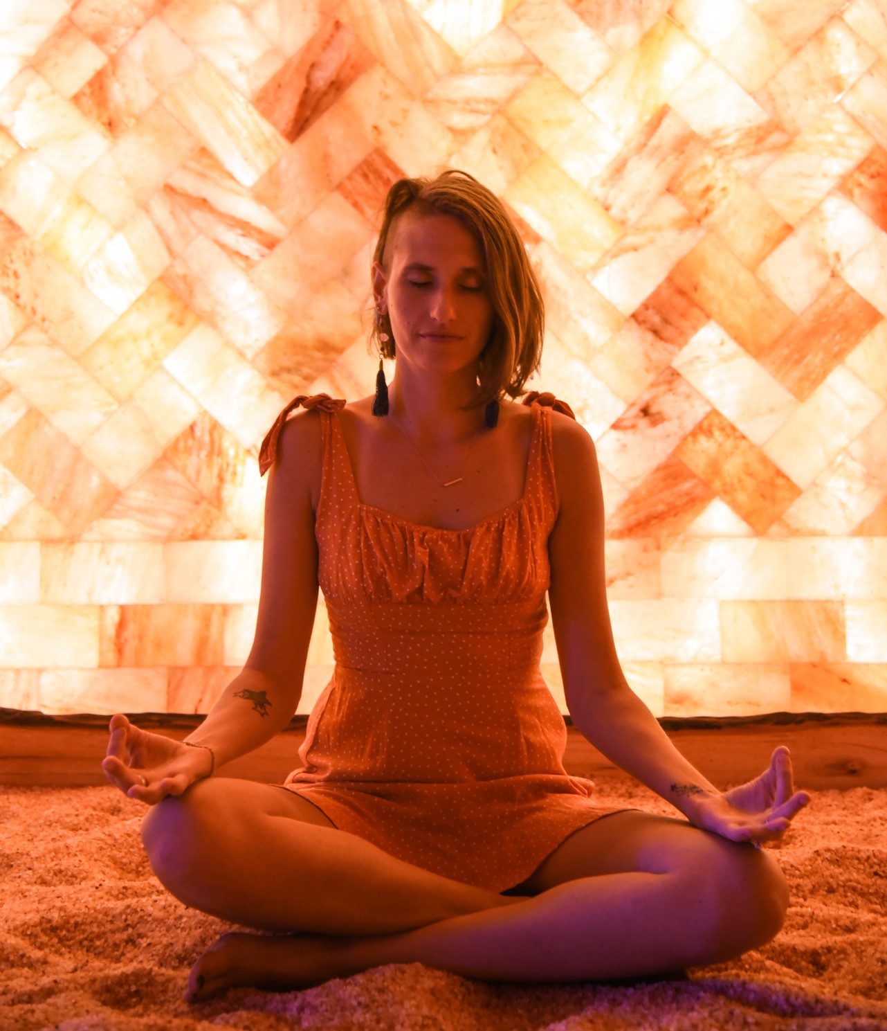 Woman Meditating On A Salt-Covered Floor In Front Of A Led Backlit Salt Panel Wall At The Prana Salt Cave - Wilmington, North Carolina.
