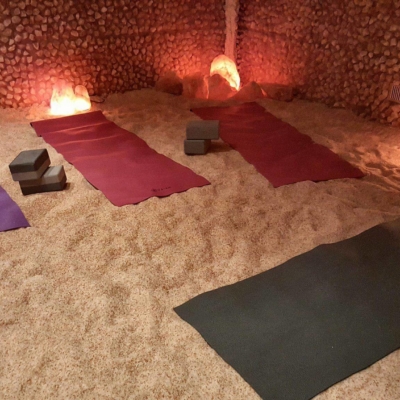 Four Yoga Mats On A Salt-Covered Floor With Lighted Himalayan Salt Stones Surrounded By Salt Panels.