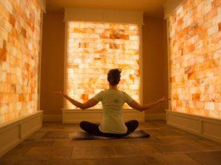 Woman Sitting On A Blanket On A Tile Floor Surrounded By Led Backlit Salt Panels At The Release Well-Being Center - Westbourough, Massachusetts.