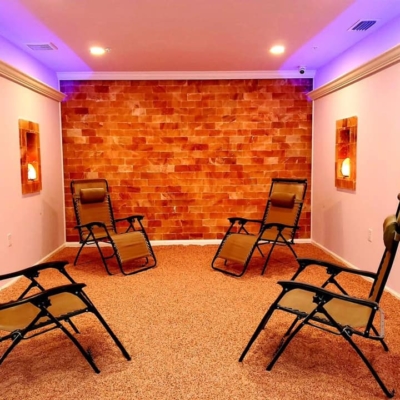 Four Chairs On A Salt-Covered Floor With Four Rectangle Salt Stone Grooves With Salt Stone Lamps In Them And A Himalayan Salt Stone Wall.