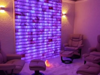 Three Tan Chairs With Ottomans In A Salt-Covered Room With A Purple Led Backlit Salt Brick Wall With A Salt Rock Lamp In The Middle Of The Room