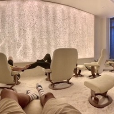 Guests Relaxing In White Cushioned Lounge Chairs In A White Room With A Salt-Covered Floor And An Led Lit Salt Wall In The Background