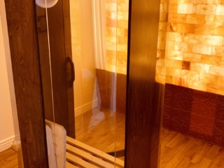 Dark Wooden And Glass Salt Booth Facing A Himalayan Salt Stone Wall Backlit By Orange Lighting.