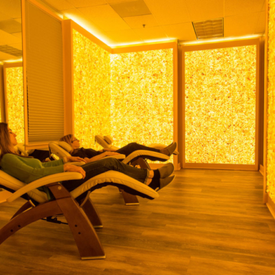 Two Women Relaxing In Reclining Chairs With A Mirror And Orange Back Lit Salt Stone Walls.