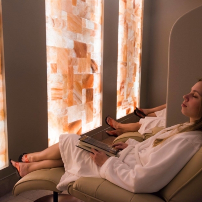 Woman in a white robe relaxing in a lounge chair facing a LED backlit salt panel wall at the Sundara Inn and Spa - Wisconsin Dells, Wisconsin.