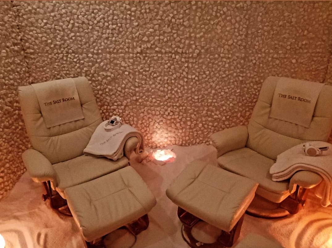 Two White Cushioned Reclining Chairs With Blankets And Headsets On A Salt-Covered Floor Surrounded By Salt Stone Walls.