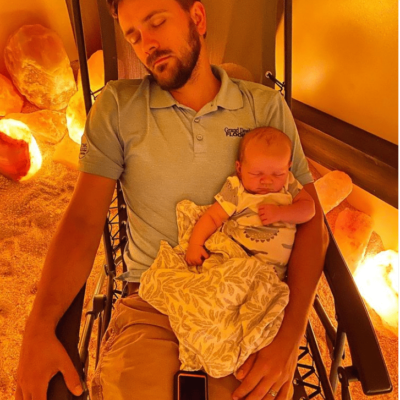 Infant rests on father while relaxing during a salt room halotherapy session at The Well On Main.