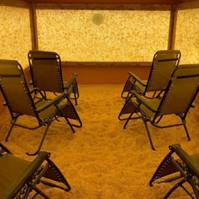 Six Reclining Chairs In A Salt Therapy Room On A Salt-Covered Floor Surrounded By A Rectangular Panel Of A White Backlit Salt Stones.