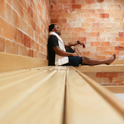 Man relaxing on a light wooden bench leaning up against a Himalayan salt panel wall at the Turnberry - Aventura, Florida.