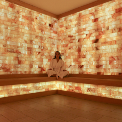 Woman relaxing on a wooden bench in a salt therapy room surrounded by LED backlit salt panel walls at the Turnberry - Aventura, Florida.