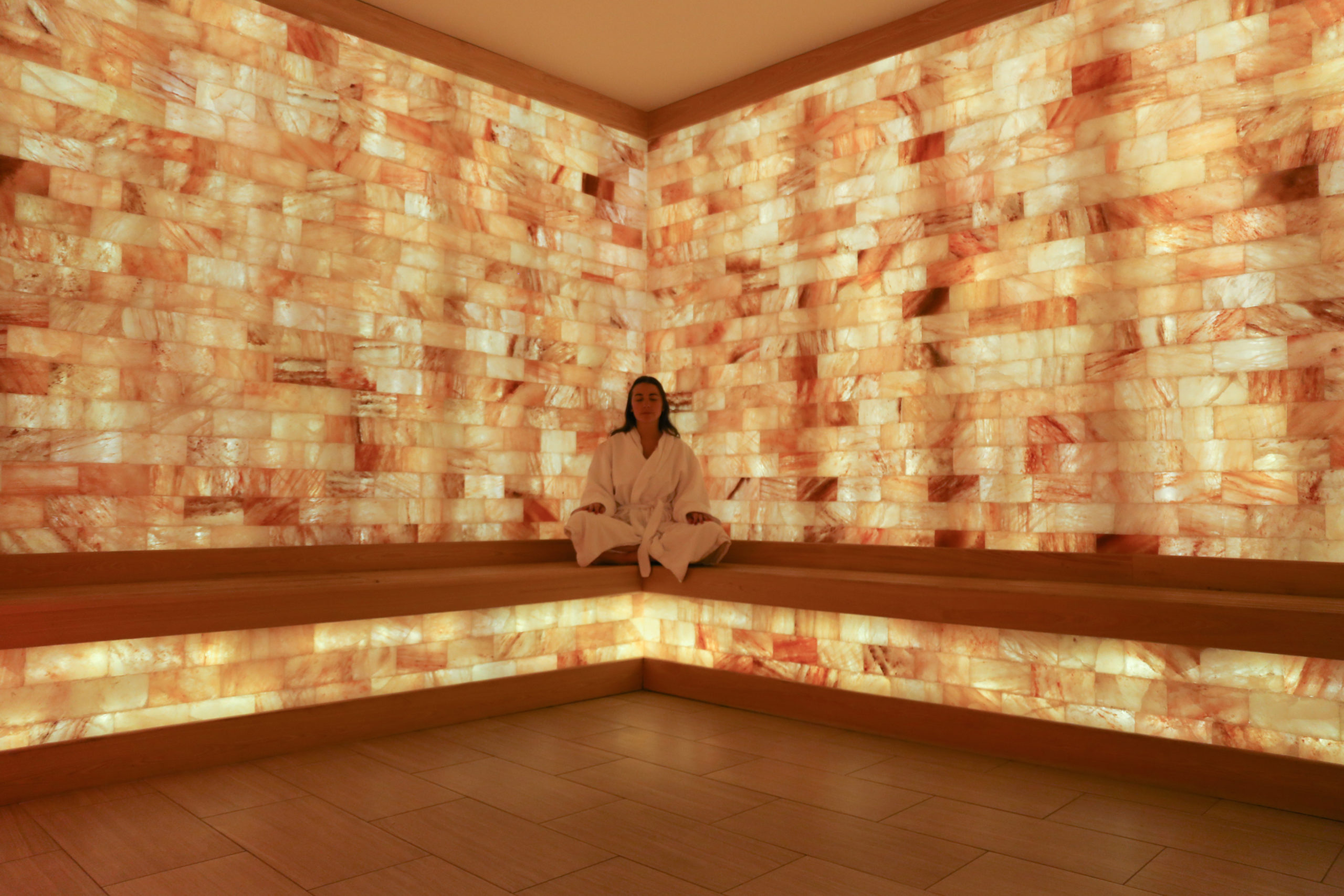 Woman Relaxing On A Wooden Bench In A Salt Therapy Room Surrounded By Led Backlit Salt Panel Walls At The Turnberry - Aventura, Florida.
