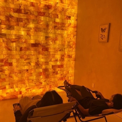 Two Women Reclined In Chairs Relaxing In Front Of A Led Backlit Salt Panel Wall With Two Butterfly Pictures On The Wall At Venus Moon Wellness Boutique - Maricopa, Arizona.