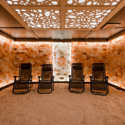 Four Brown Reclining Mesh Chairs On A Salt-Covered Floor In A Himalayan Salt Stone Chamber Backlit With White Lighting At The Villa Harrah In Lake Tahoe, Nv