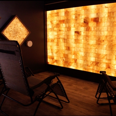 Three Brown Reclining Chairs On A Brown Wooden Floor Facing An Orange Backlit Paneled Salt Wall With Two Diamond Shaped Salt Stone Décor.