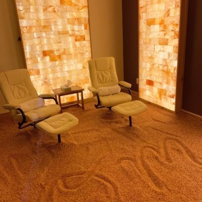 Two White Cushioned Chairs With Foot Rets On A Salt-Covered Floor With Two Himalayan Salt Stone Panels Backlit With Orange Lighting.