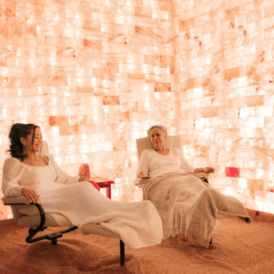 Two Women Relaxing In Reclined Chairs On A Salt-Covered Floor Surrounded By White Led Backlit Salt Panels At Wellcome Om Integral Healing &Amp; Education Center - Spring Hill, Florida.