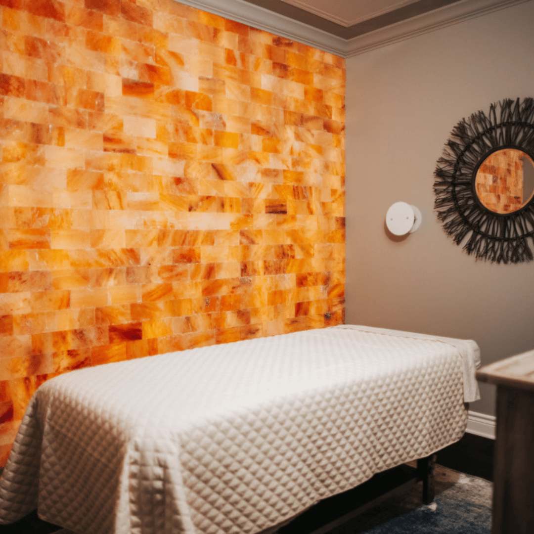The salt room at The Woodhouse Day Spa in Dallas, Texas, with a massage table and Himalayan salt brick wall with a halotherapy machine.