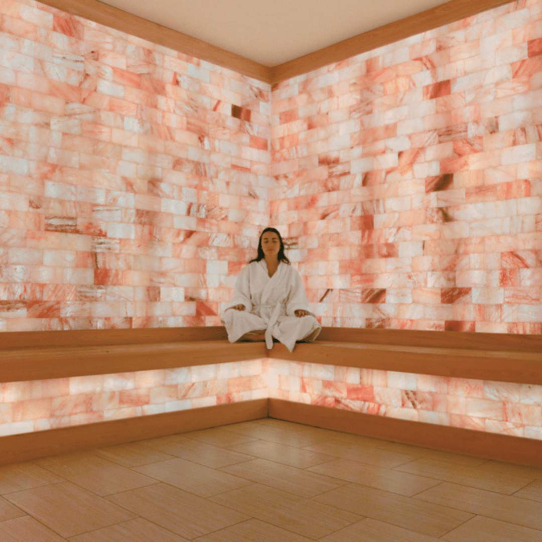 A woman sitting in a salt room on a bench in front of a Himalayan salt brick wall at the JW Marriott Miami Turnberry Resort & Spa in Aventura, Florida.