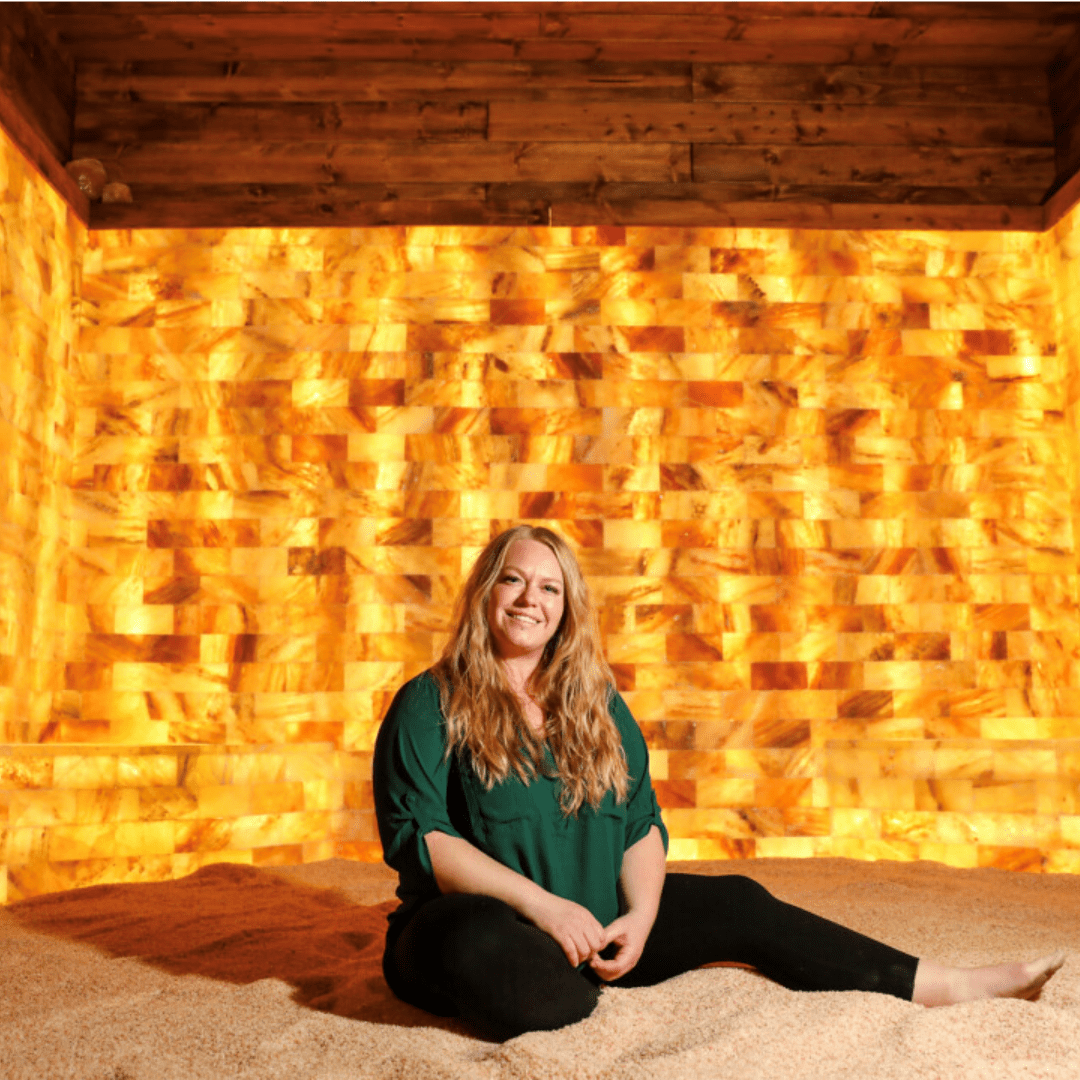 Woman sitting in a salt room in front of a Himalayan salt wall with Himalayan salt bricks.